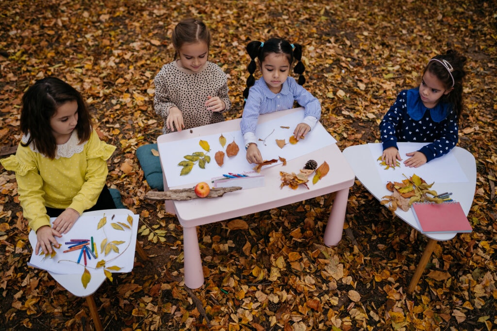 Four young girls organize leaves on small tables