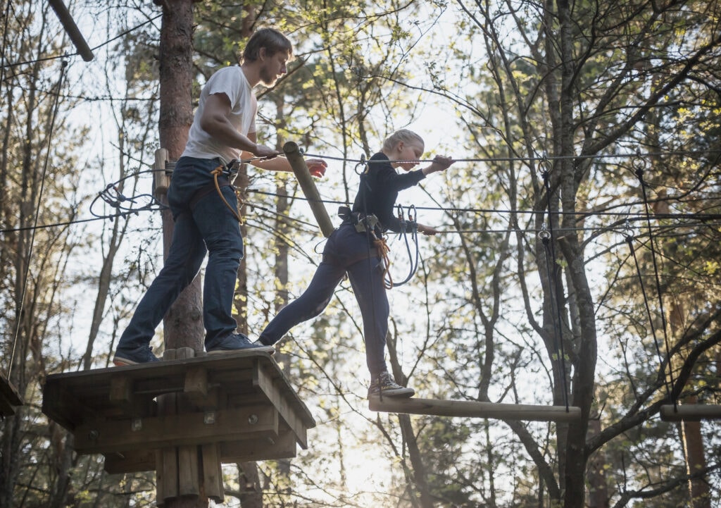 A man coaches his daughter on a ropes course up in the trees
