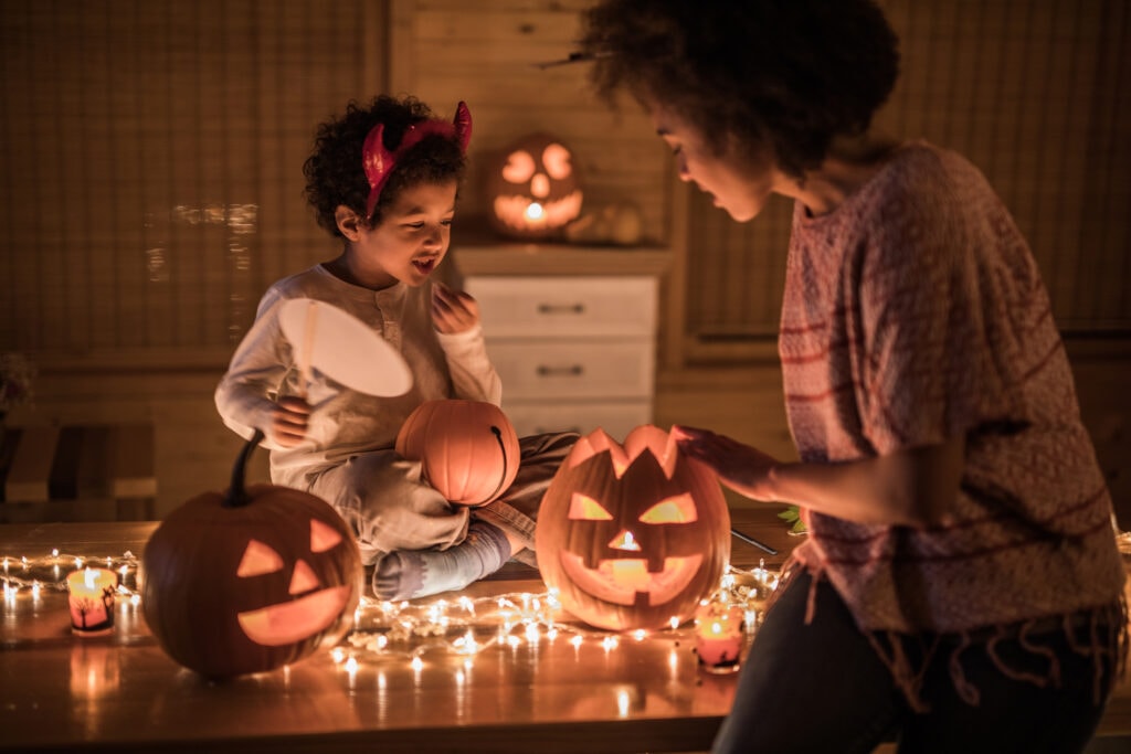 A mother and child arrange some jack-o-lanterns and string lights
