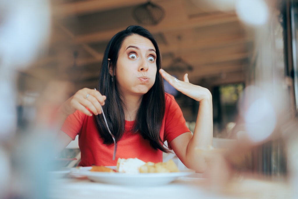 A woman at a table surprised at how spicy her food is