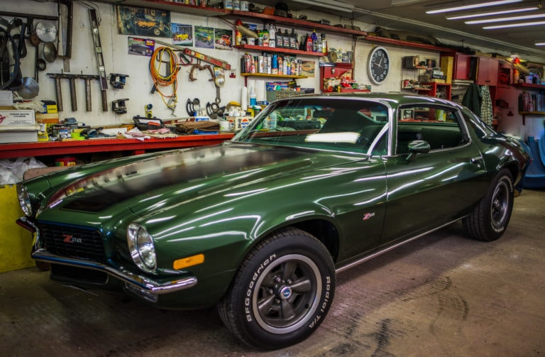 Classic green car parked inside a garage workshop with tools on the wall.