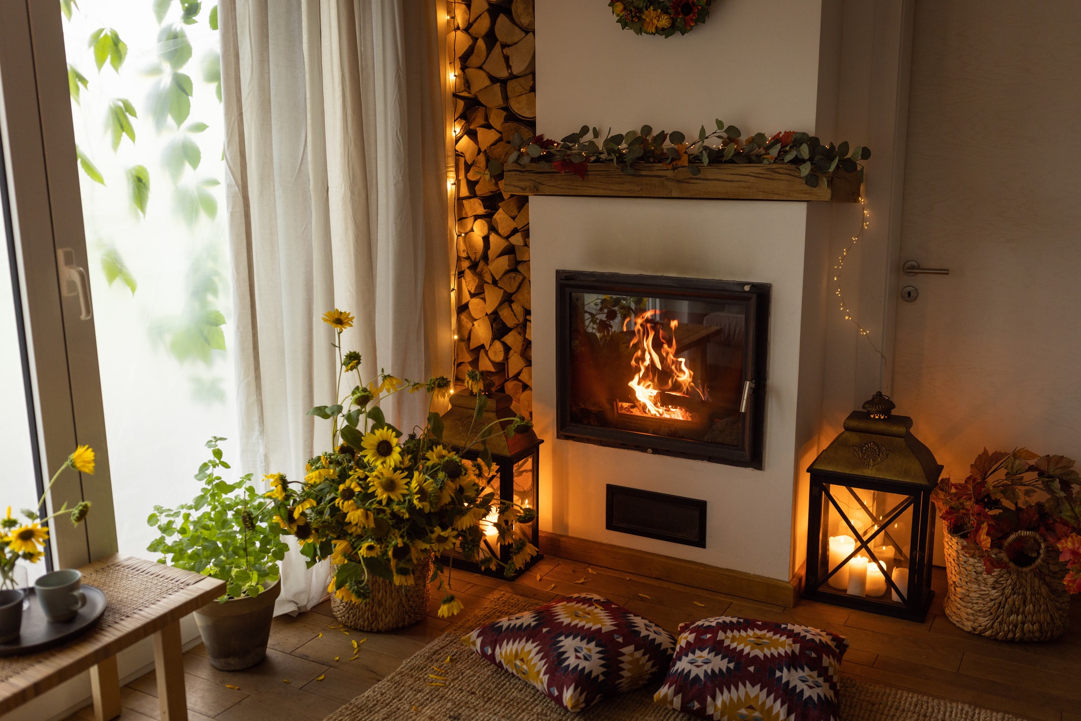 Cozy living room with a lit fireplace, decorative lanterns, flowers, and warm ambient lighting.