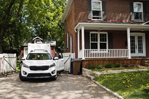 Car parked in a driveway beside a brick house with people entering or exiting.
