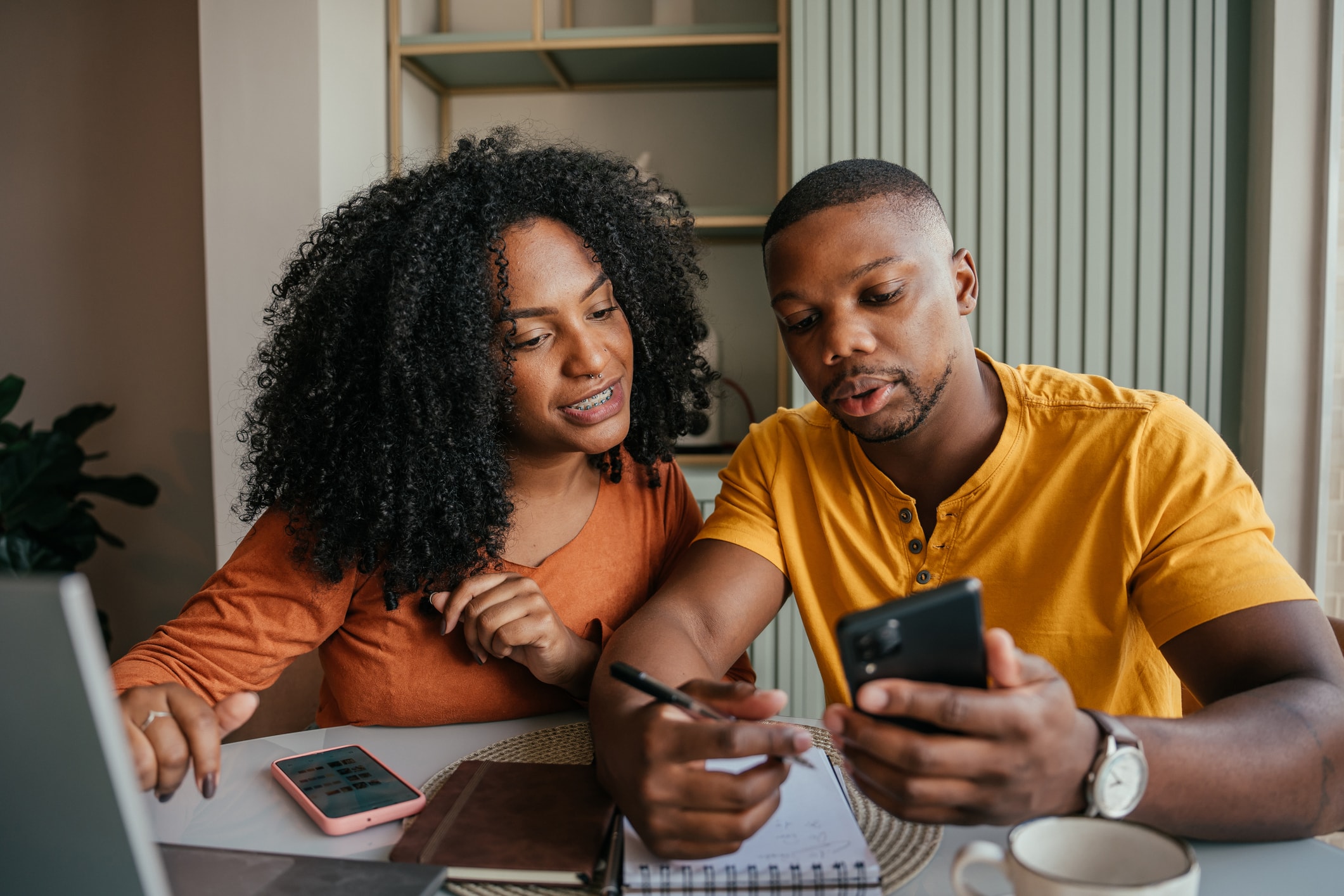 Two people reviewing a phone and taking notes at a table.
