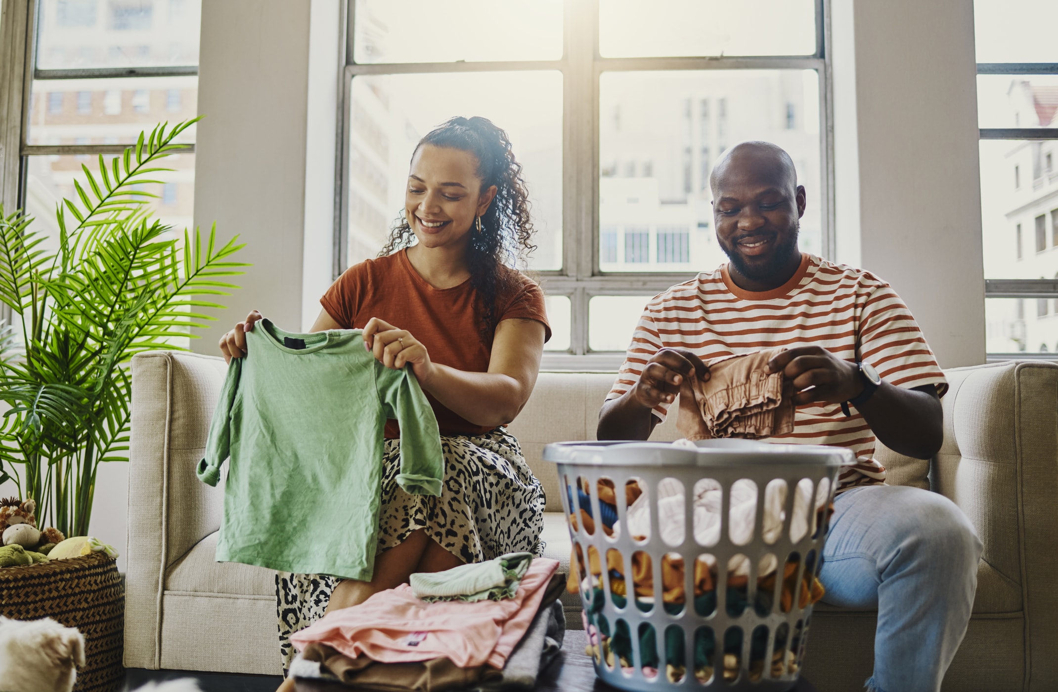 Two people folding laundry together on a couch with a basket of clothes.
