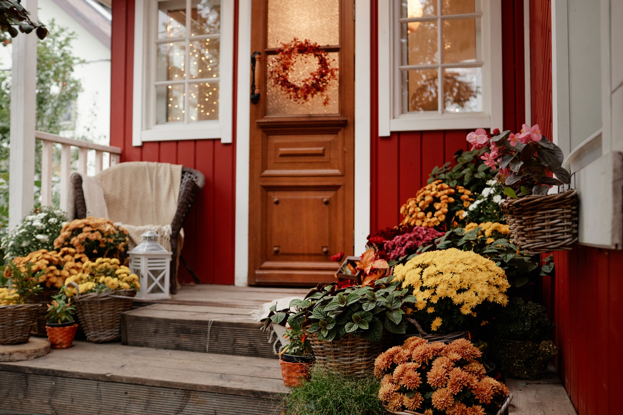 Welcoming front porch of a red house decorated with colorful potted flowers, a seasonal wreath, and cozy outdoor accents.
