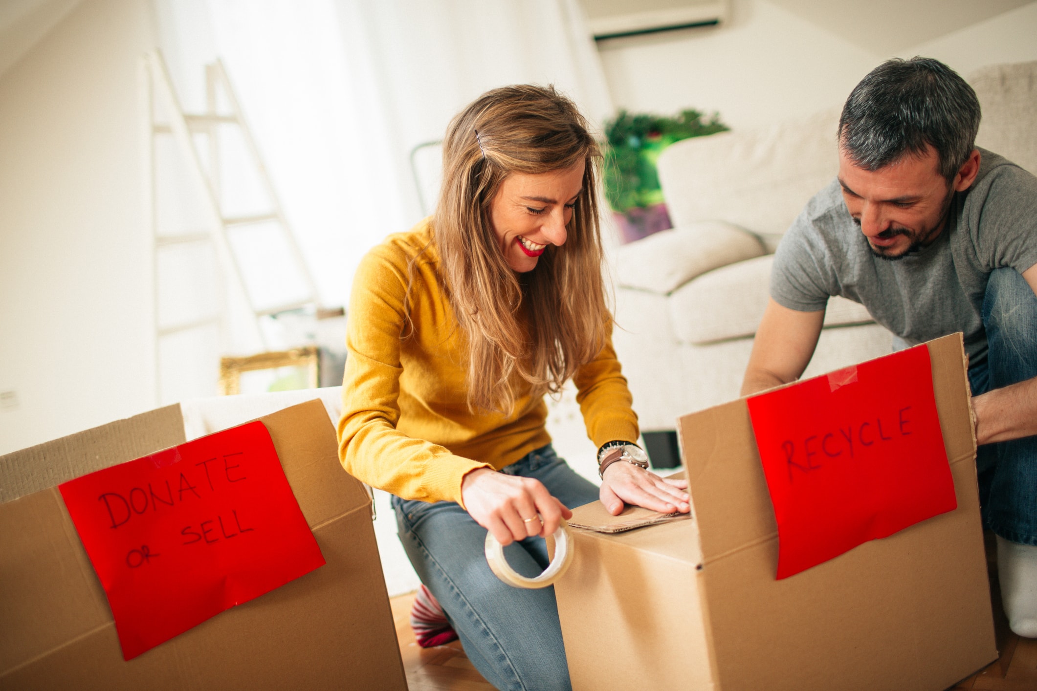 Person packing boxes labeled “donate or sell” and “recycle” at home.
