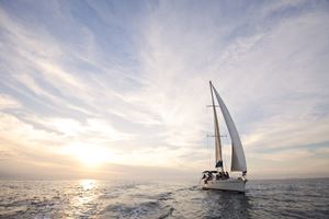 Sailboat navigating on the water at sunset with its mainsail fully unfurled.