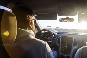 Person driving a car during sunset, viewed from the back seat.