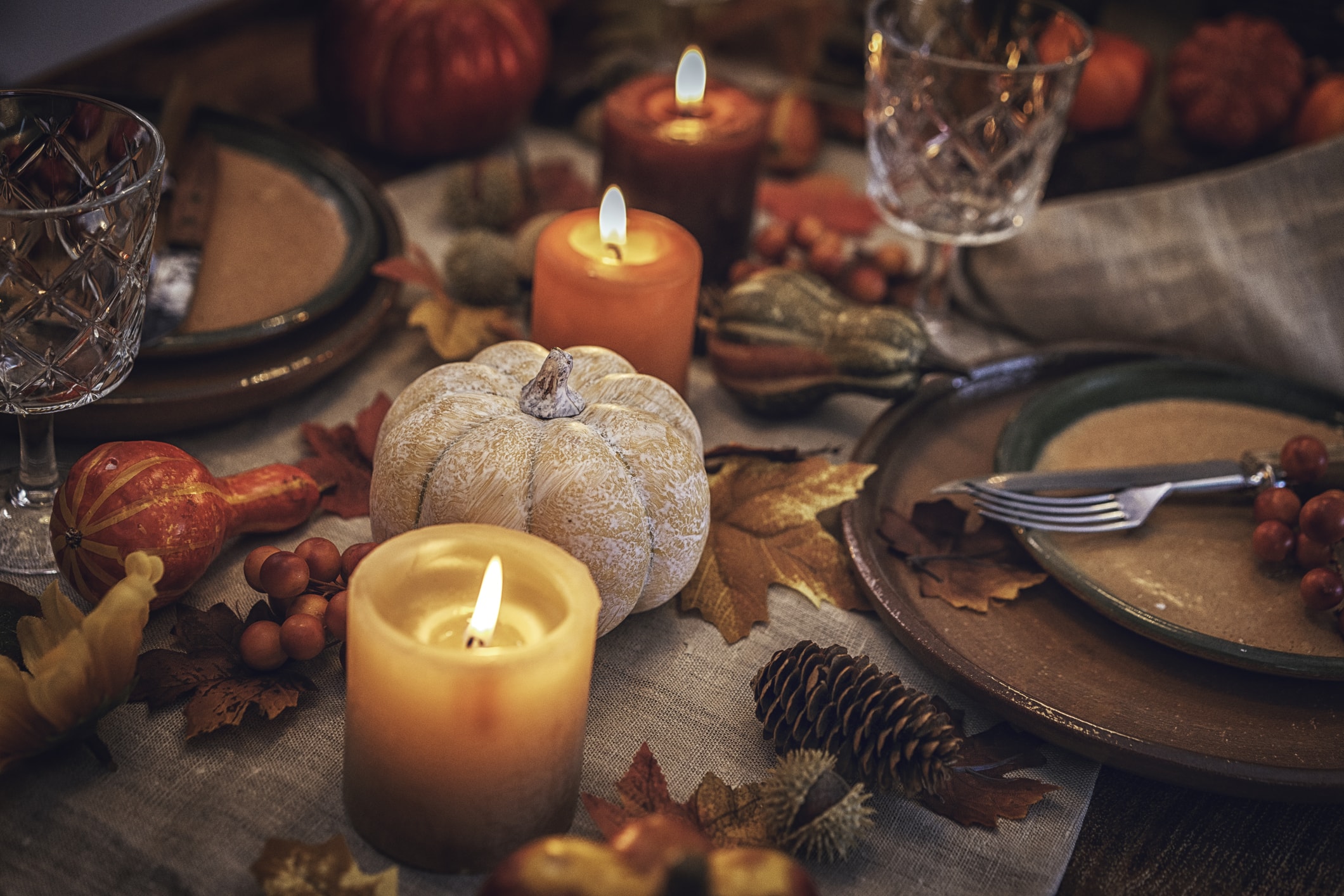 Autumn-inspired table setting featuring lit candles, decorative pumpkins, fall leaves, and place settings arranged for a seasonal gathering.