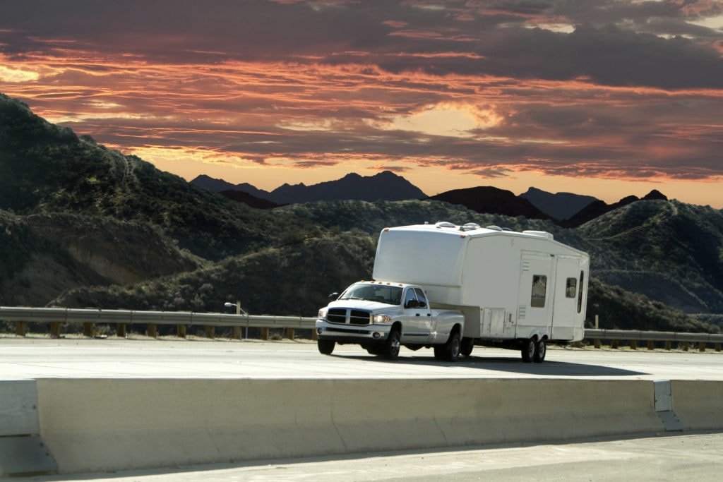 A pick-up truck towing a camper trailer on a highway.