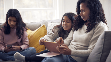 Personne assise sur un canapé avec deux enfants, utilisant des appareils numériques dans un salon.