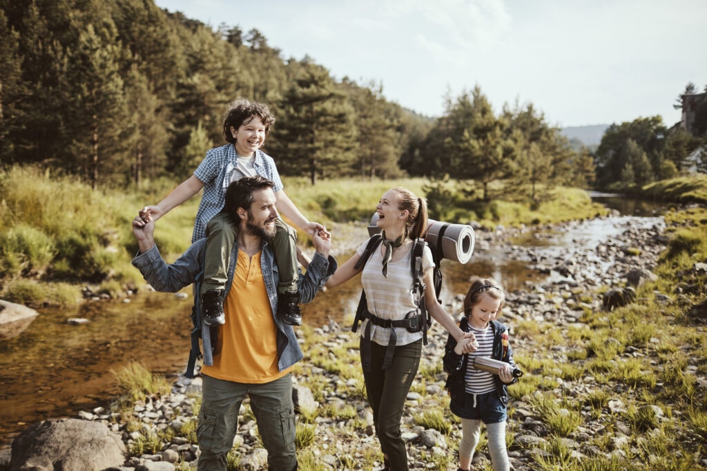 A boy, sitting on his father's shoulders, along with a mother and daughter, hike by a stream