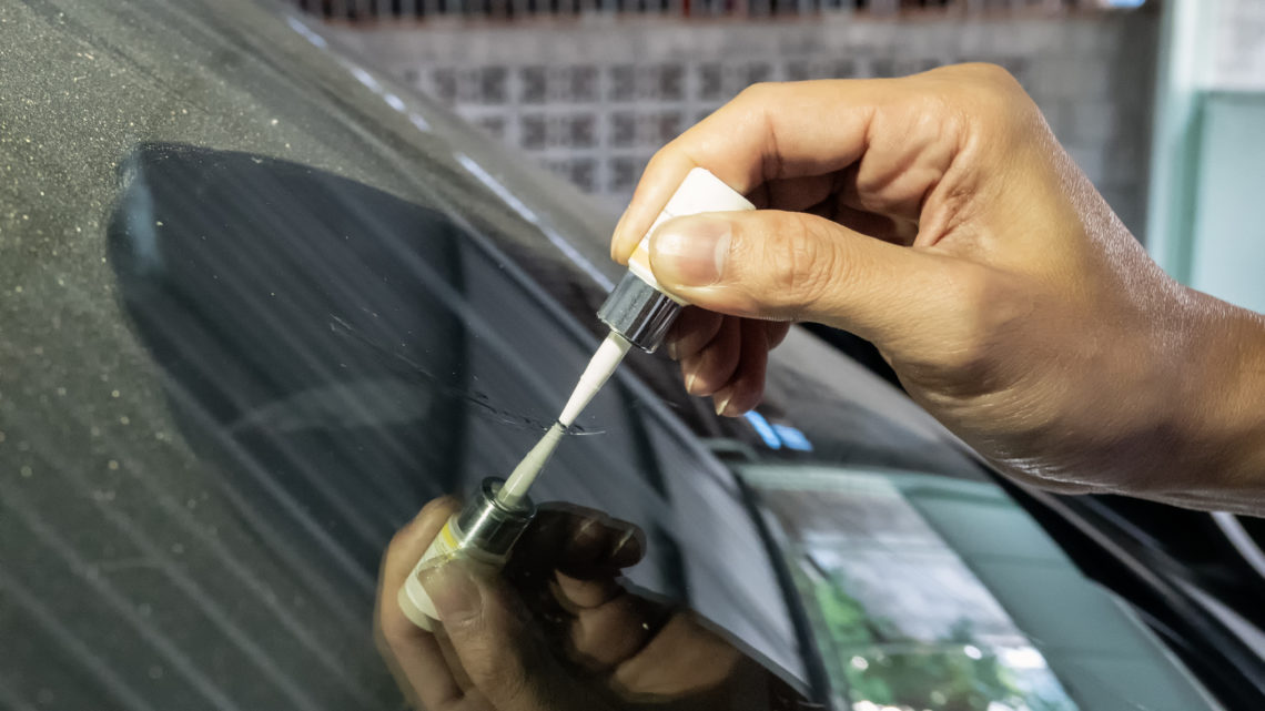 An automotive technician applies adhesive to a car windshield