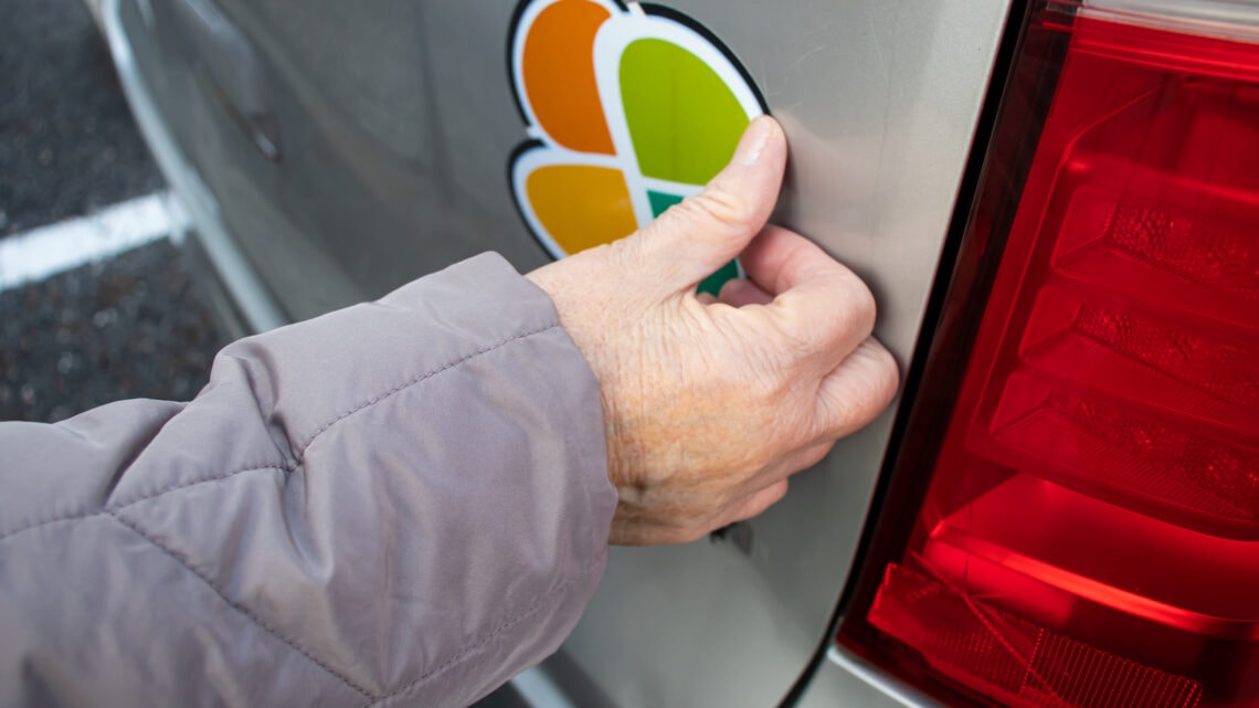 A hand removing a sticker from the trunk lid of a car.
