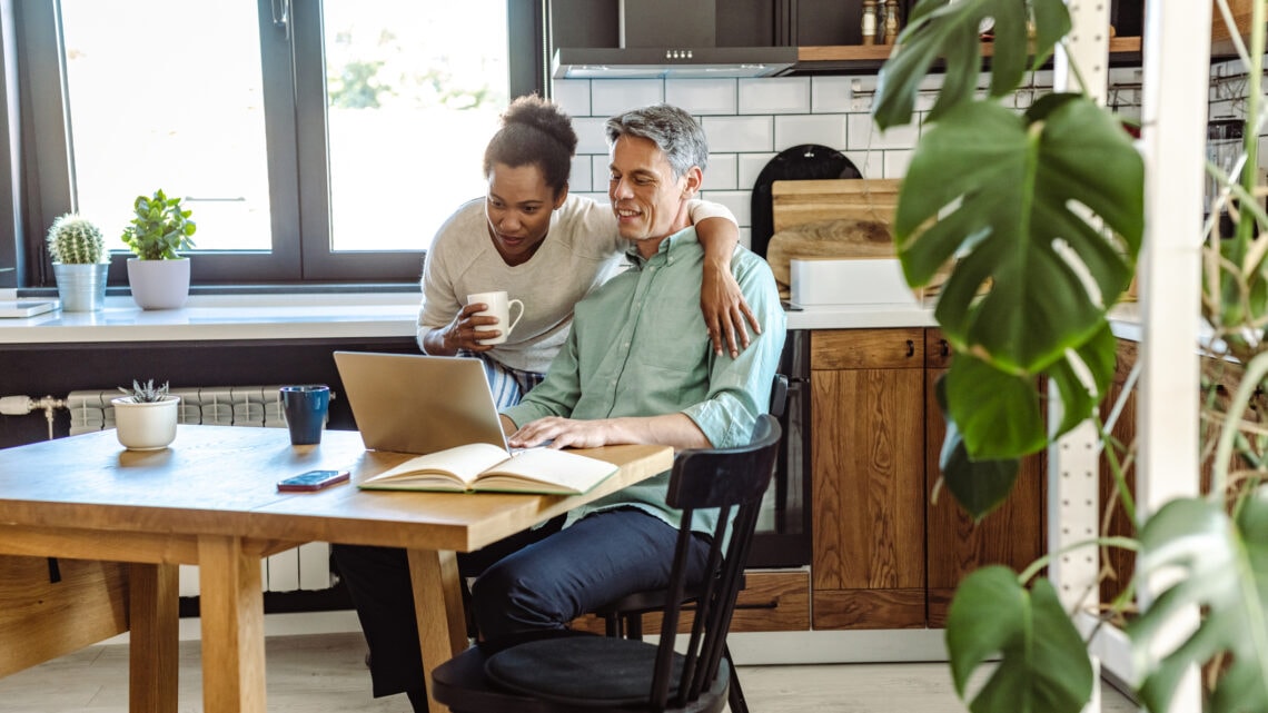 A man and woman review their insurance policy on a laptop at their kitchen table