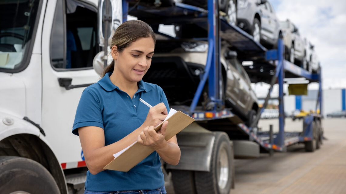 A woman checking a list standing beside a vehicle carrier.