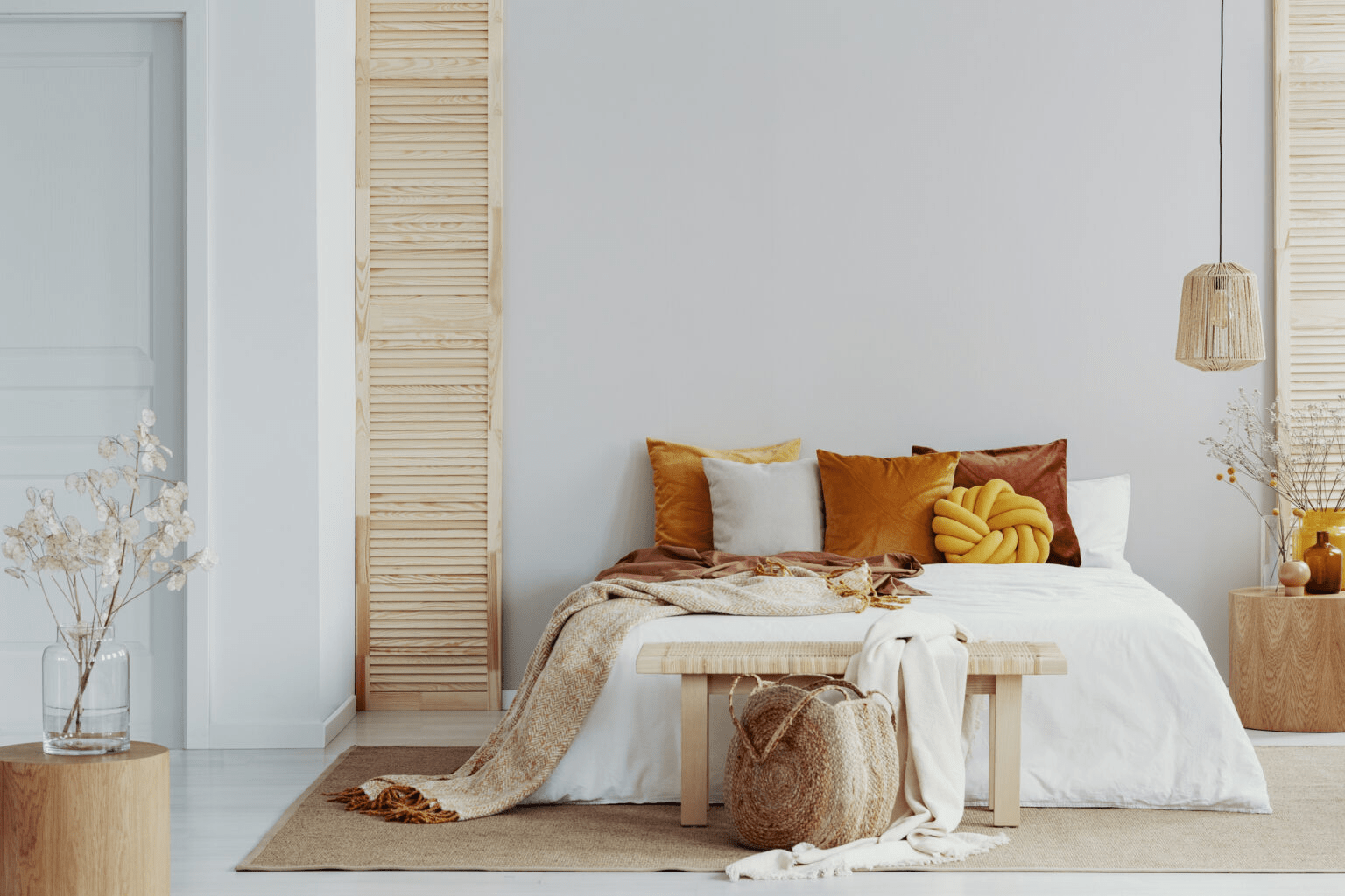 Bright, cozy bedroom with a neatly made bed, warm-toned accent pillows, woven décor, and natural wood finishes.
