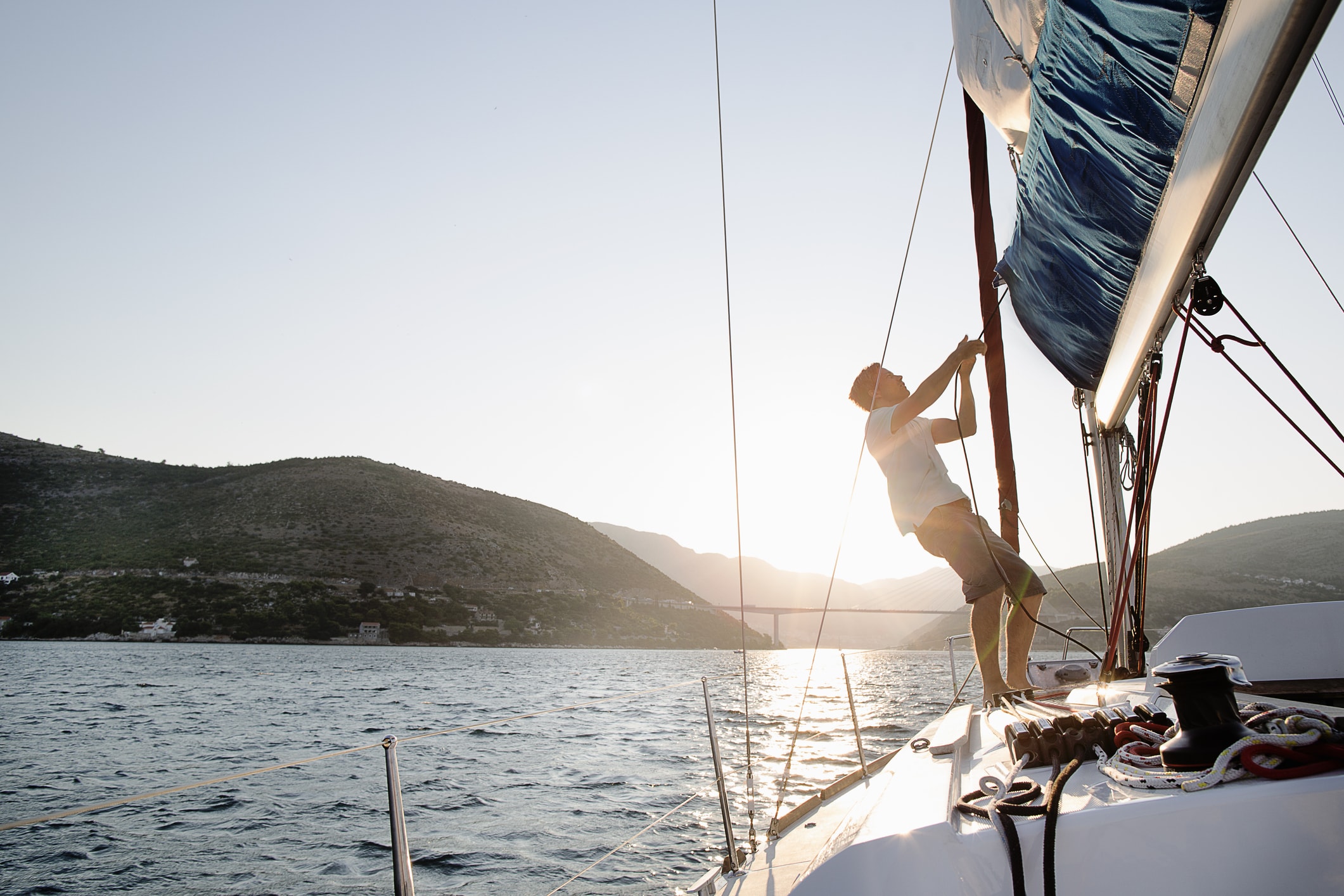 Personne ajustant une voile sur un bateau au coucher du soleil près de la côte. Provide your feedback on BizChat