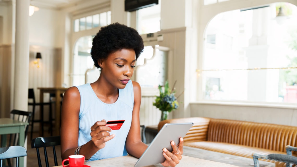 Une femme effectuant un achat en ligne tient une carte de crédit et une tablette