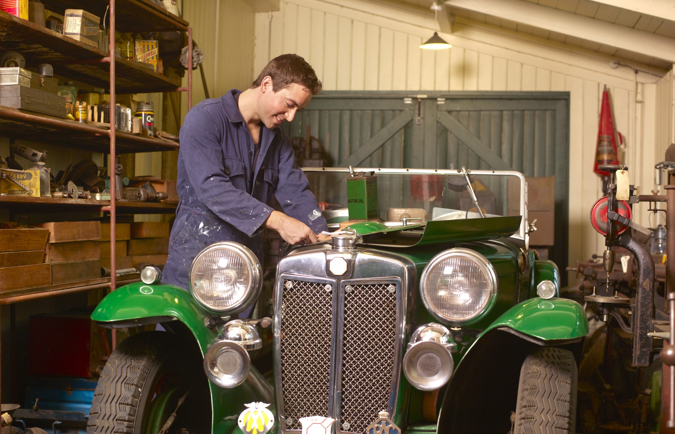 A man working on a classic car engine in a garage workshop.