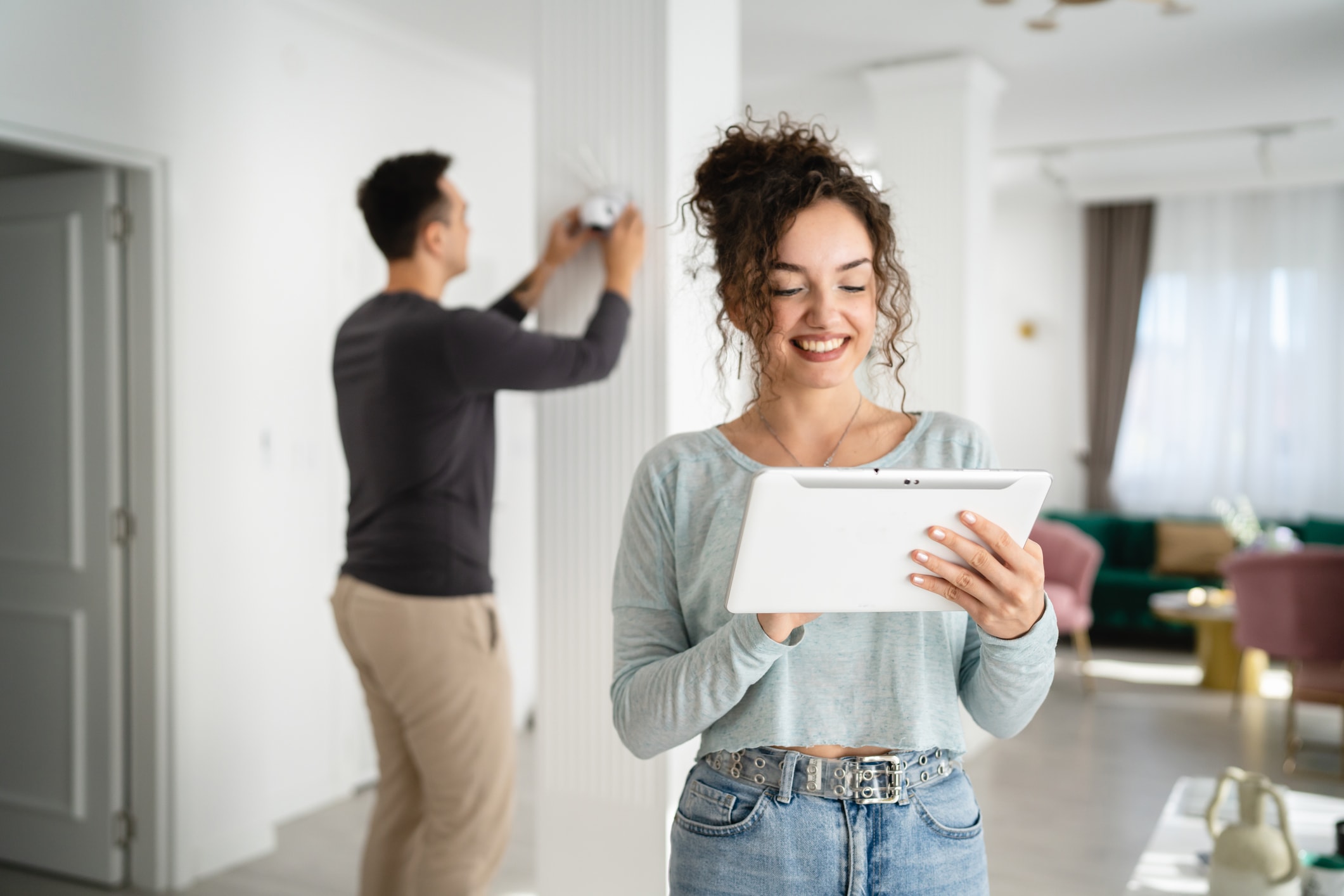 Person using a tablet while another person installs a device on the wall at home.