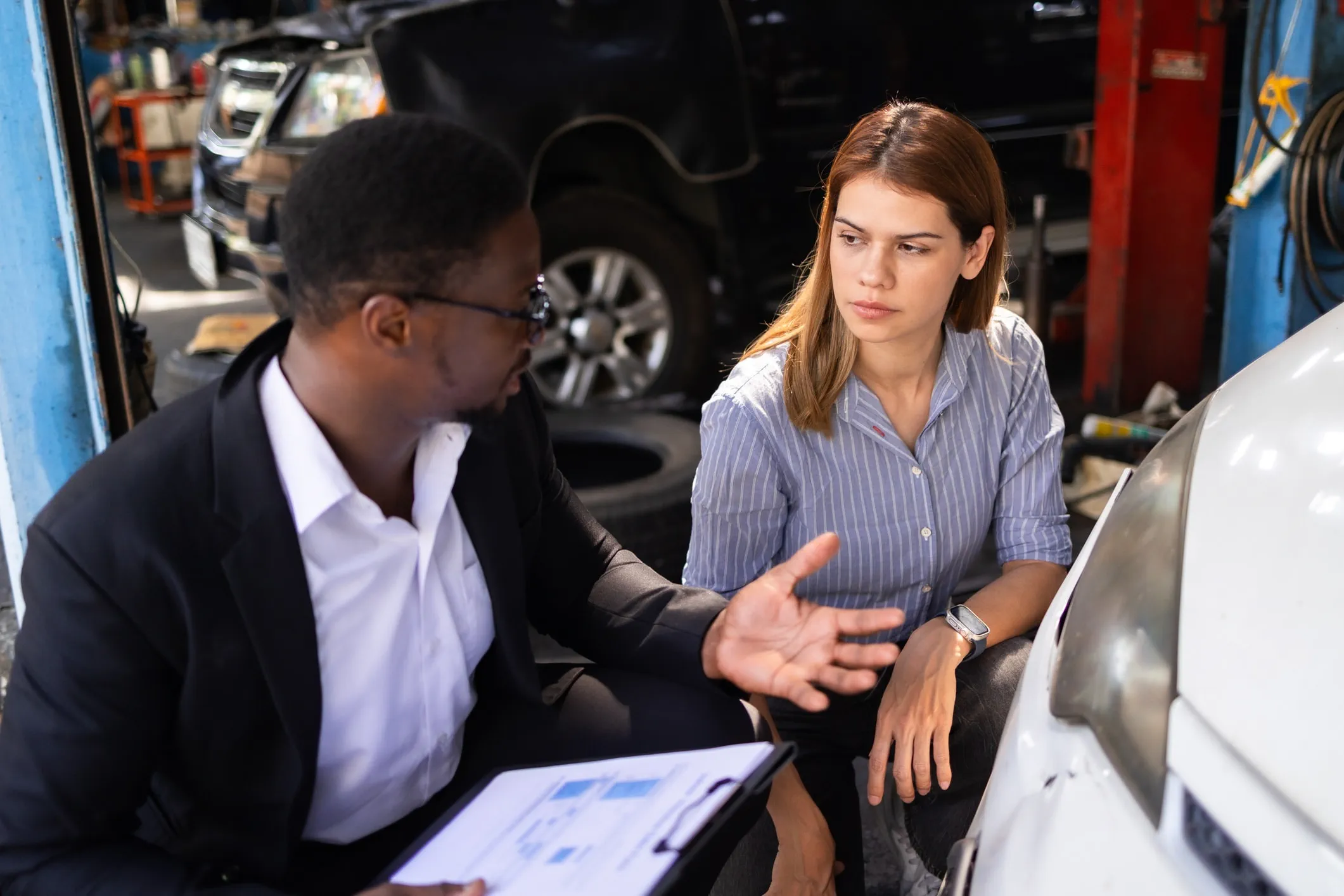 Two people reviewing documents beside a car in an auto repair shop.