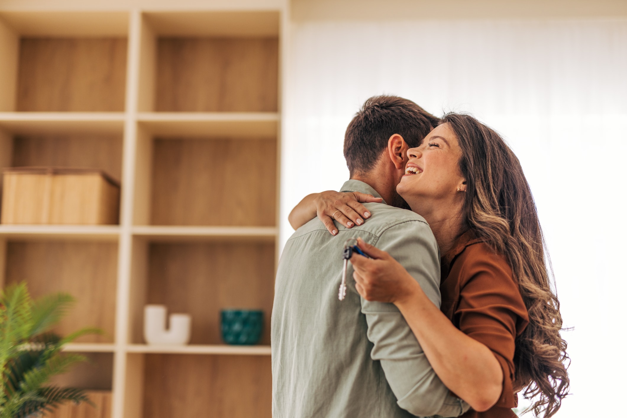 Two people hugging indoors while holding a set of house keys.