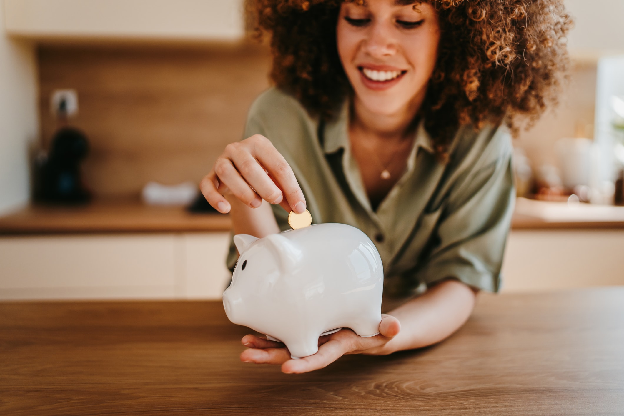 Person placing a coin into a white piggy bank on a table.