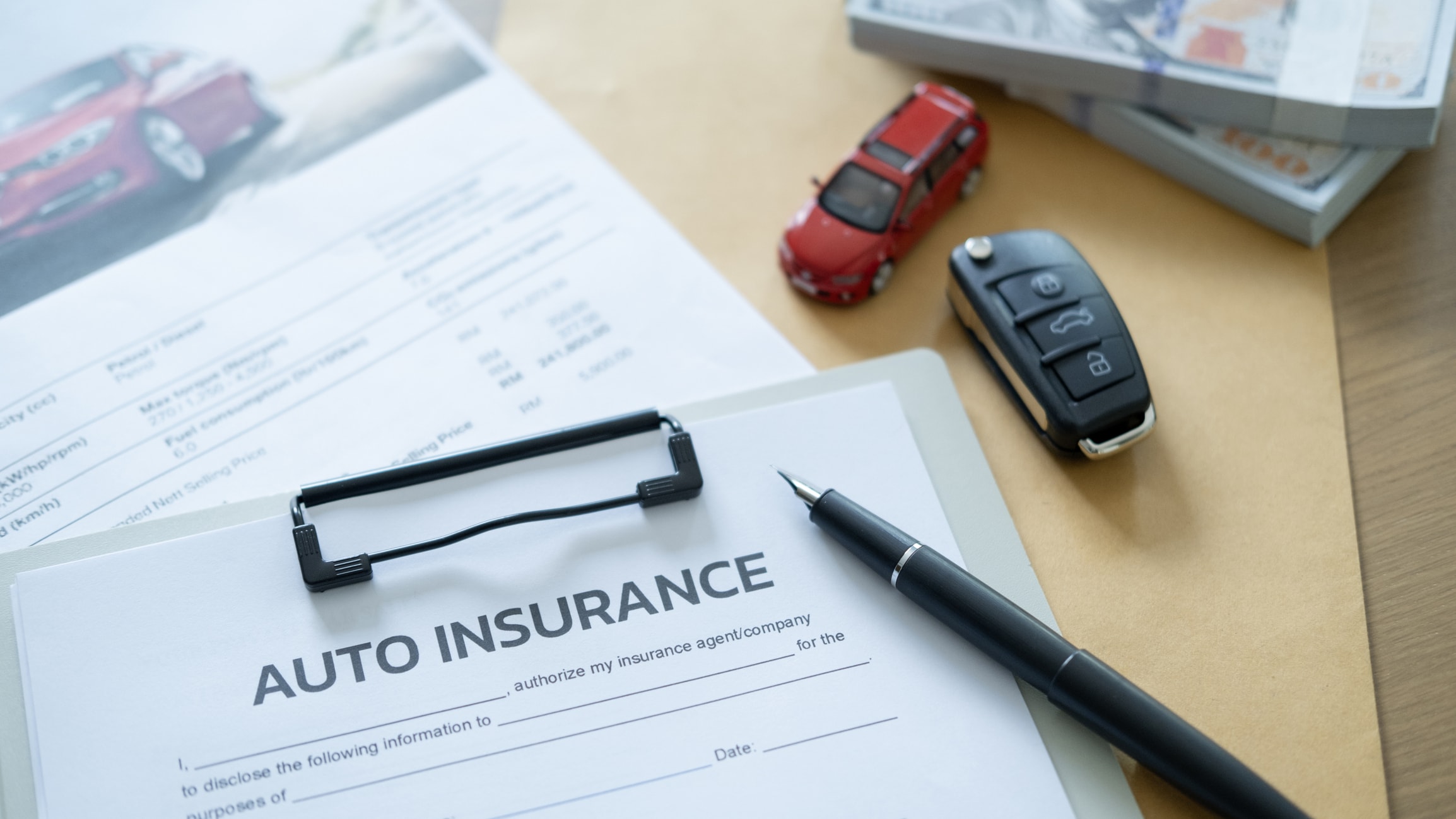Auto insurance form with car key, pen, cash, and a small model car.