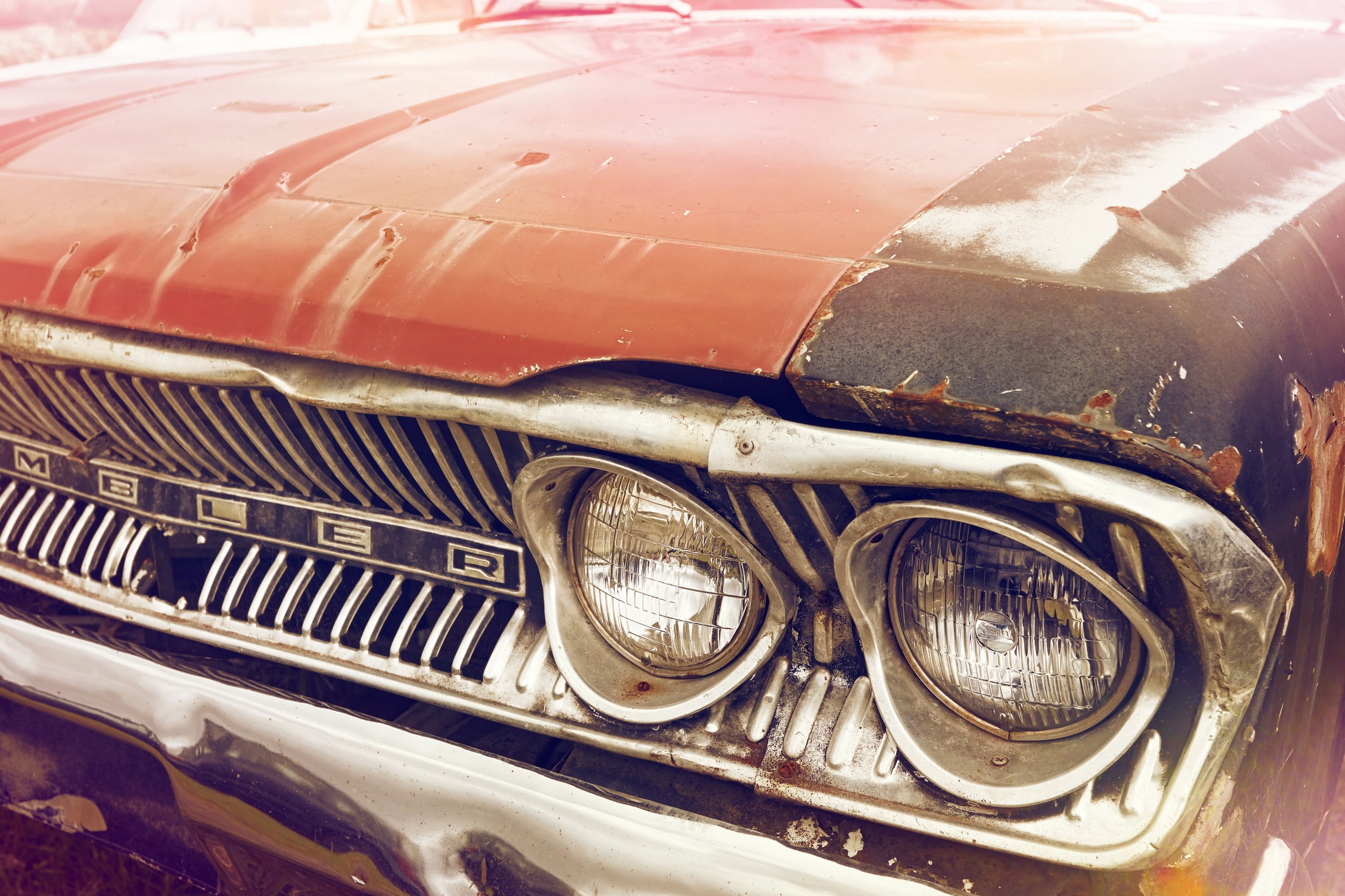 Close-up of a rusty vintage car front with dented hood and headlights.
