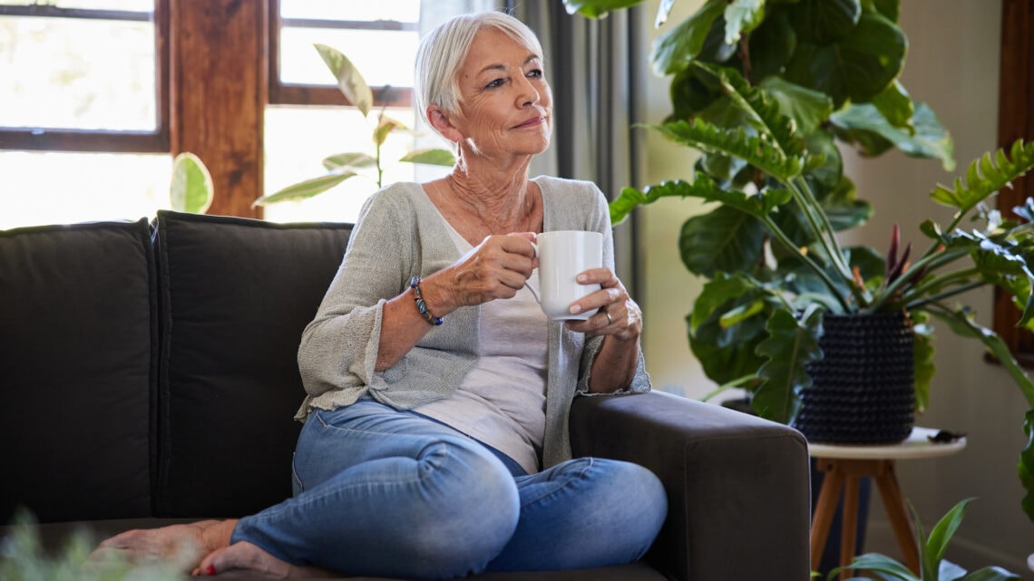 An older woman sitting on a couch with a cup of coffee