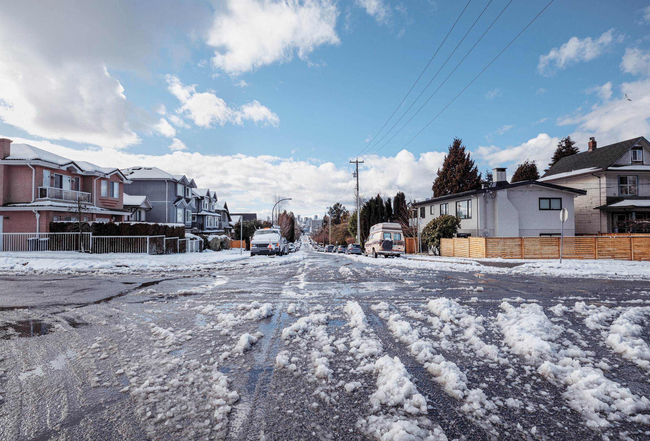 Snow-covered residential street with slush and parked cars.