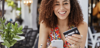 a woman smiling while holding a phone and a credit card