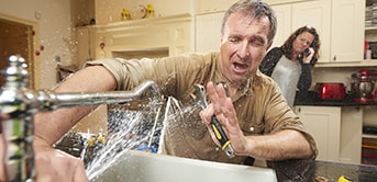 man trying to fix a broken faucet while getting splashed