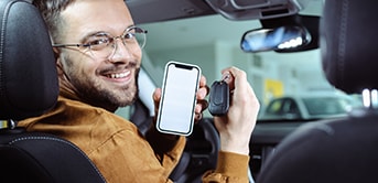 a man wearing glasses holding a phone and keys in a car