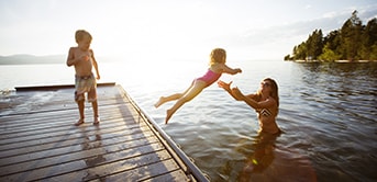 little girl jumping into the water into the arms of her mother while another child looks on