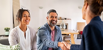 A smiling couple shaking hands with their agent