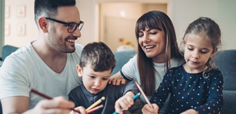 parents sitting on a couch with two children colouring