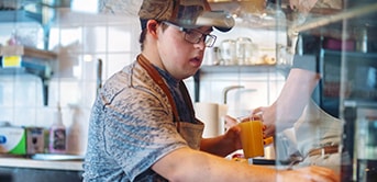 a man in a cap and apron holding a glass of orange juice