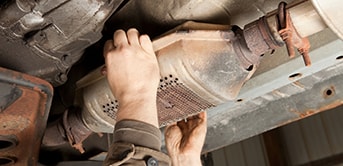 a close-up of a man stealing a catalytic converter of a car