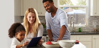 a little girl, woman and a man looking at a tablet in a kitchen